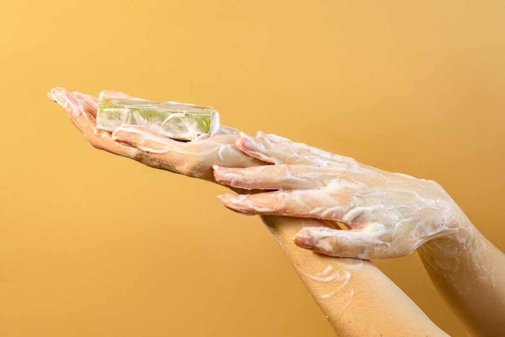 Hands covered in foamy soap, representing hygiene and cleanliness against a vibrant yellow background.